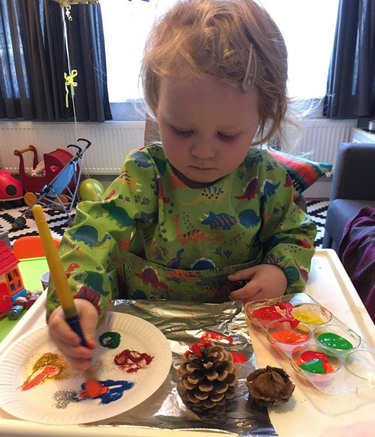 A child in an overall using bright paints and glitter to decorate a paper plate during an activity
