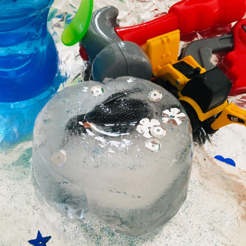 A toy penguin frozen in a circular block of ice, ready to be thawed out as a part of a child's messy play activity.