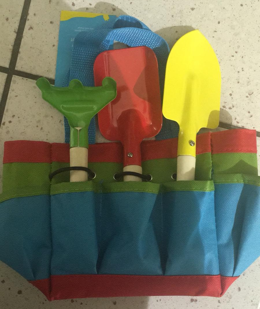 A set of child's garden tools - a green rake, a red spade and a yellow trowel - in a multicoloured utility belt.