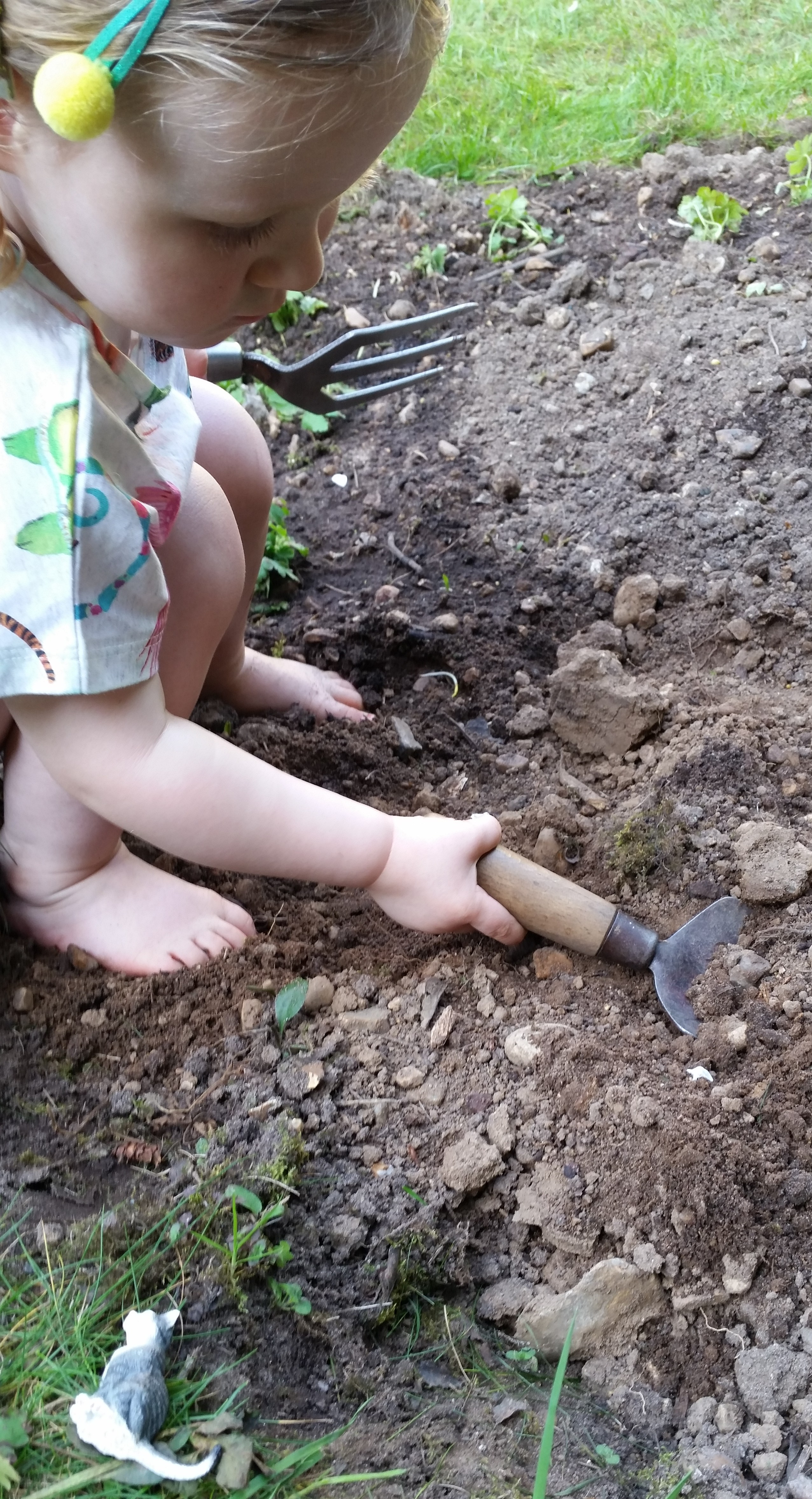 A young child crouches in a flower bed using a trowel during a gardening activity