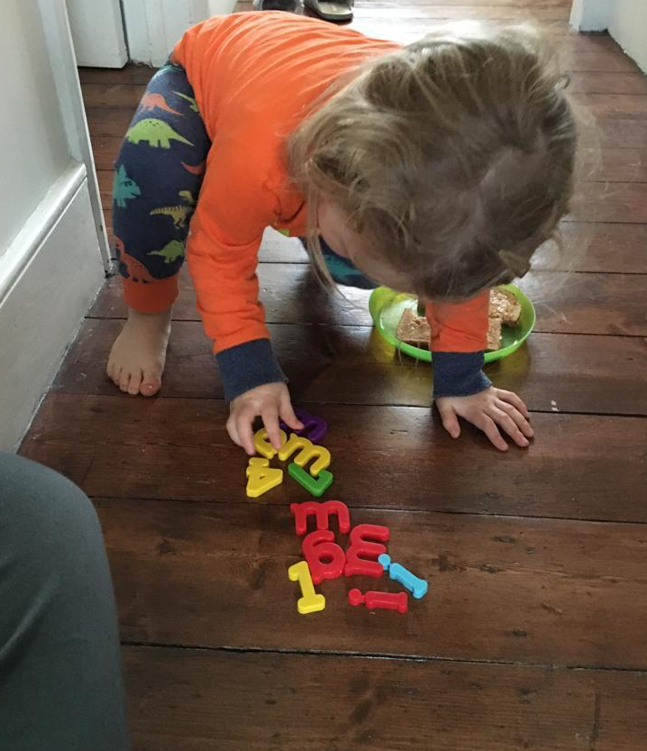 A child sorts through a selection of magnetic fridge letters on the floor.