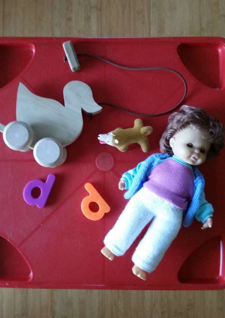 A selection of toys beginning with an initial 'd' sound - duck, dog, doll - depicted on a child's table