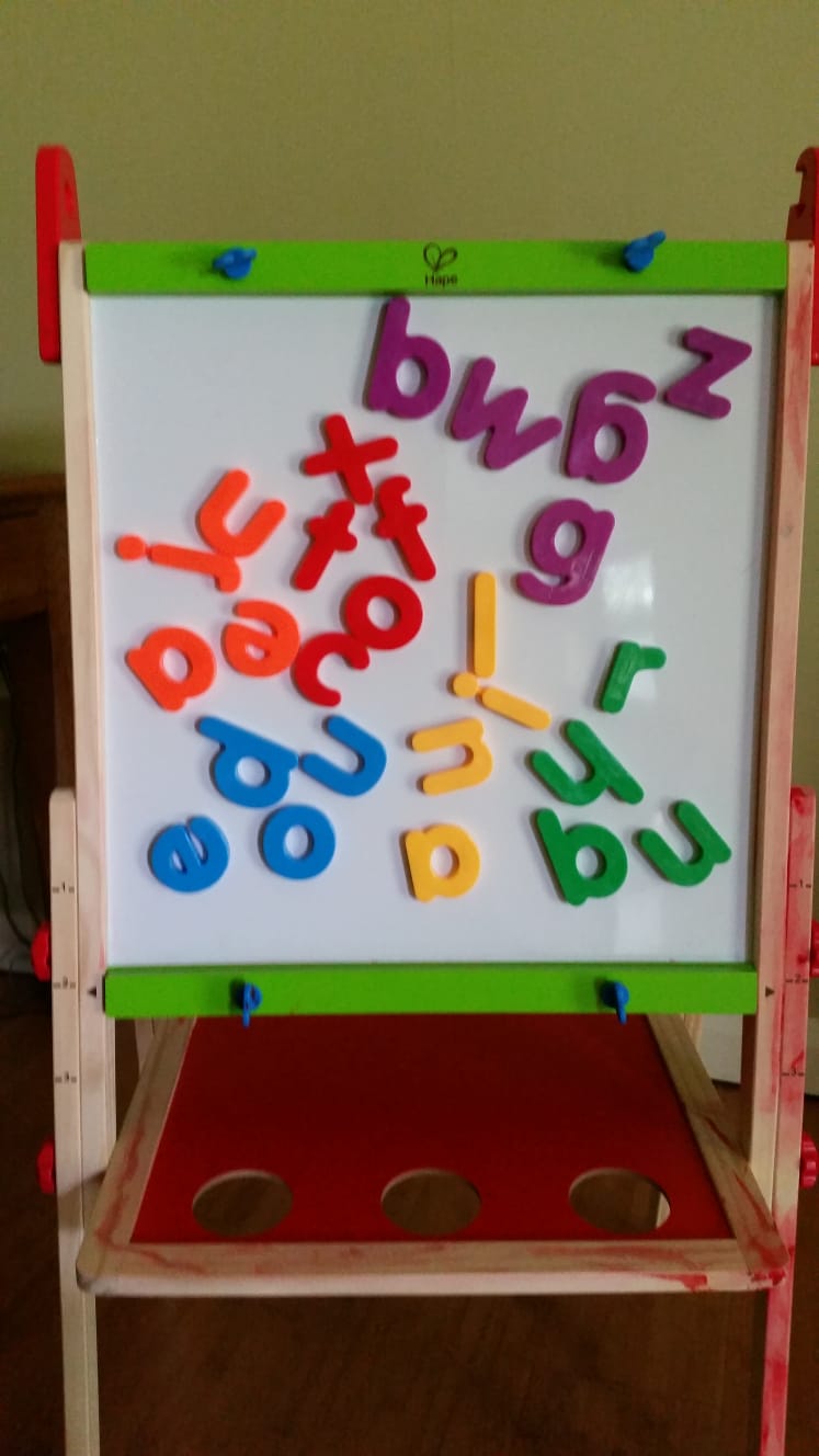 A child's easel with a set of magnetic letters arranged on it by colour.