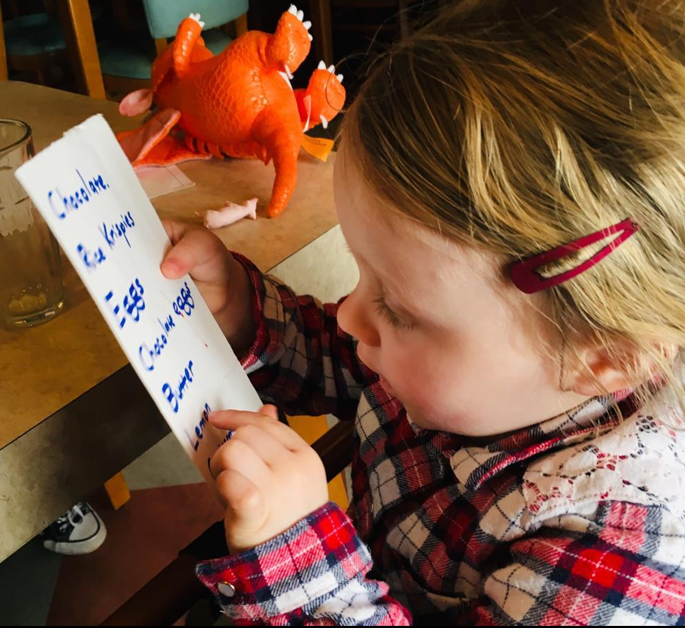 A young child runs her finger down a shopping list as part of a numeracy and literacy activity.