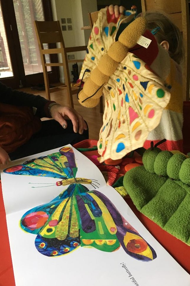 A child plays with a soft-toy caterpillar while reading The Very Hungry Caterpillar by Eric Carle