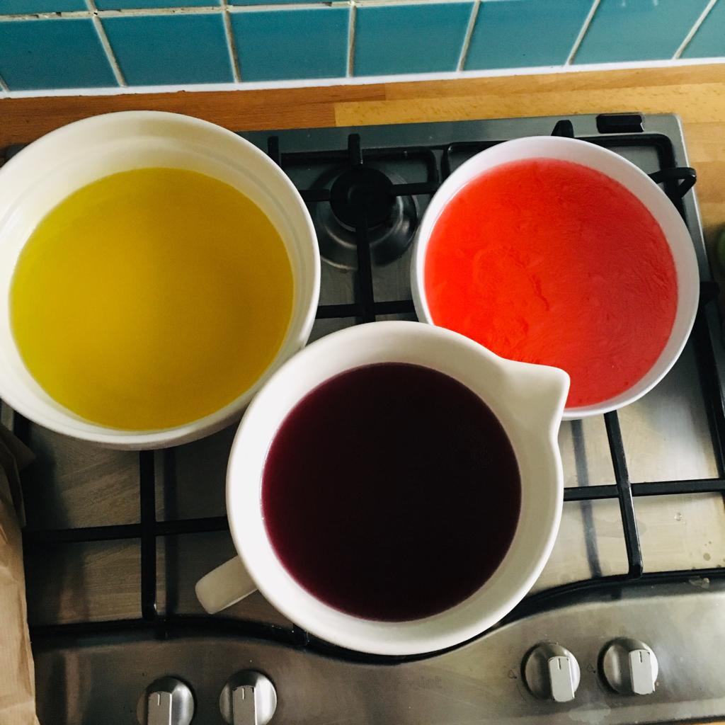Three large bowls, red, purple and amber, of jelly sitting on a stove top, ready for a messy play activity.