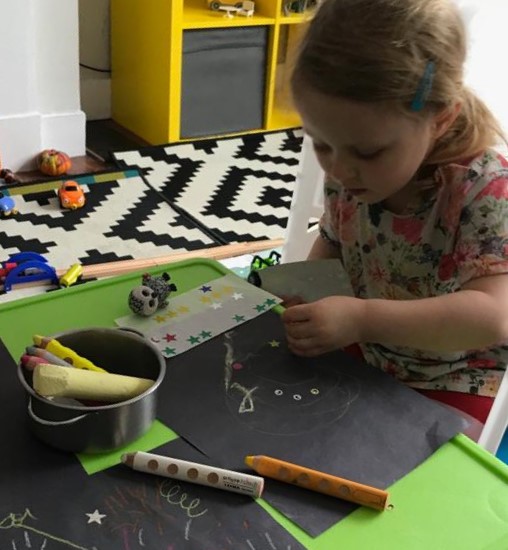 A child using chalks, large pencil crayons and star stickers on a page of black sugar paper as part of an activity