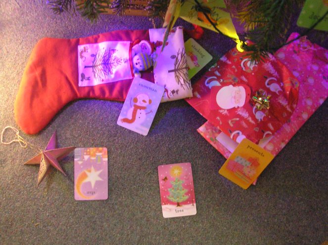 A series of child's Christmas themed flash cards are shown next to Christmas stocking and some gifts beneath a Christmas tree