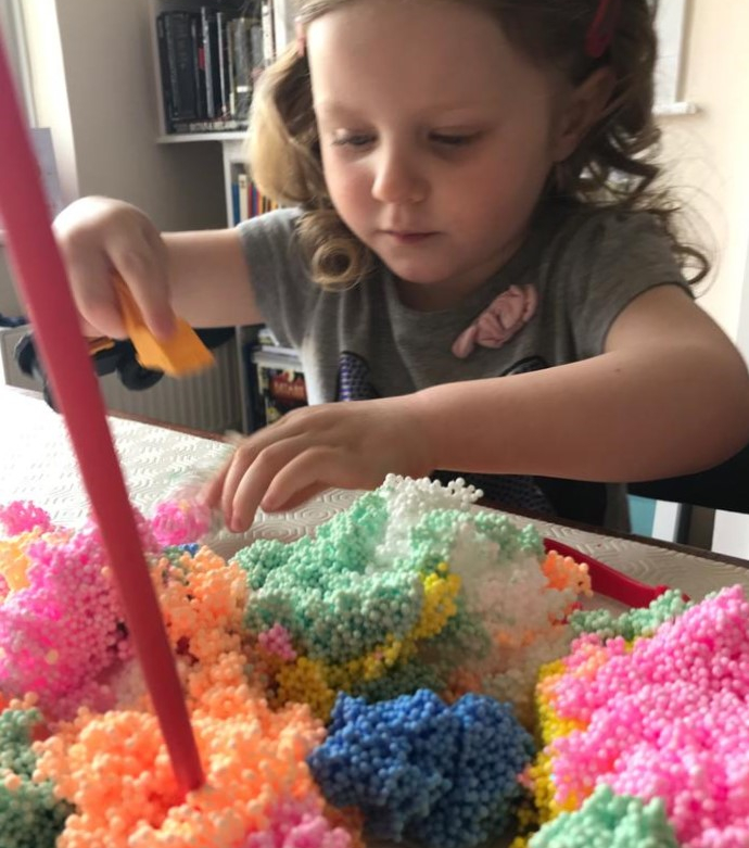A young girl using multicoloured play foam and straws for a session of messy play.