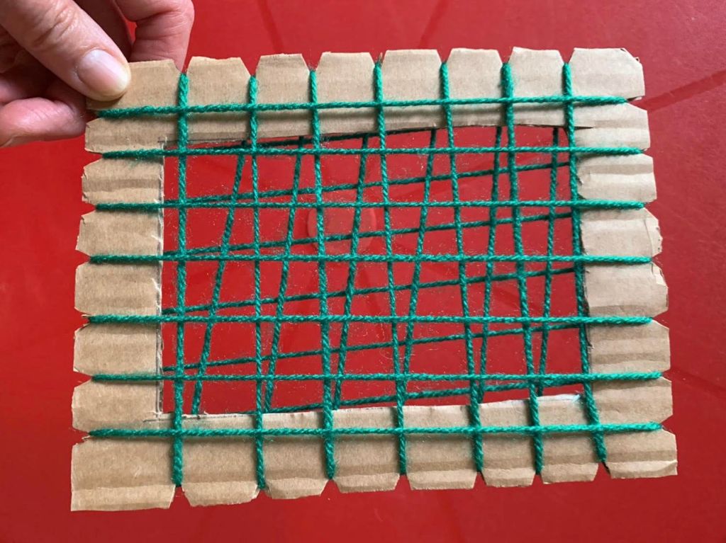 A homemade weaving frame made from cardboard and green twine