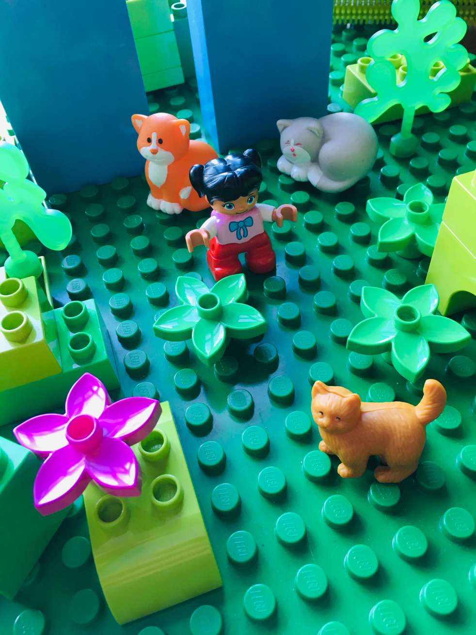 A garden made of Duplo, with a small Duplo girl surrounding by toy cats