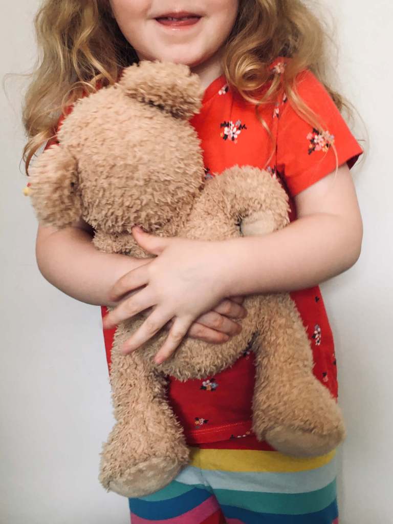 A young girl smiles and hugs her teddy bear