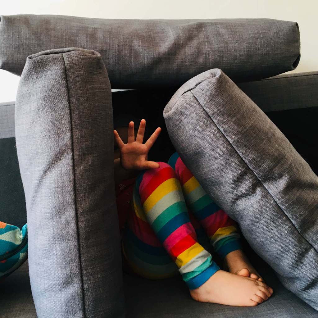 A child hides herself within a 'pillow fort' and holds her palm out to make it clear she wants to be left alone