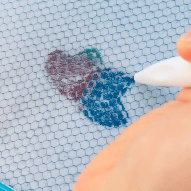 A child's overlays two heart-shaped stamps to create an image of a butterfly on a magnetic drawing board
