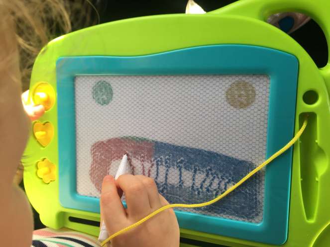 A child's draws a face on a magnetic drawing board, rendering the eyes and lips using a circular stamps and the teeth with her stylus