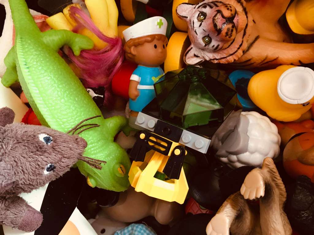 The cluttered contents of a toy box - lego, plastic animals, cuddly toys and dolls