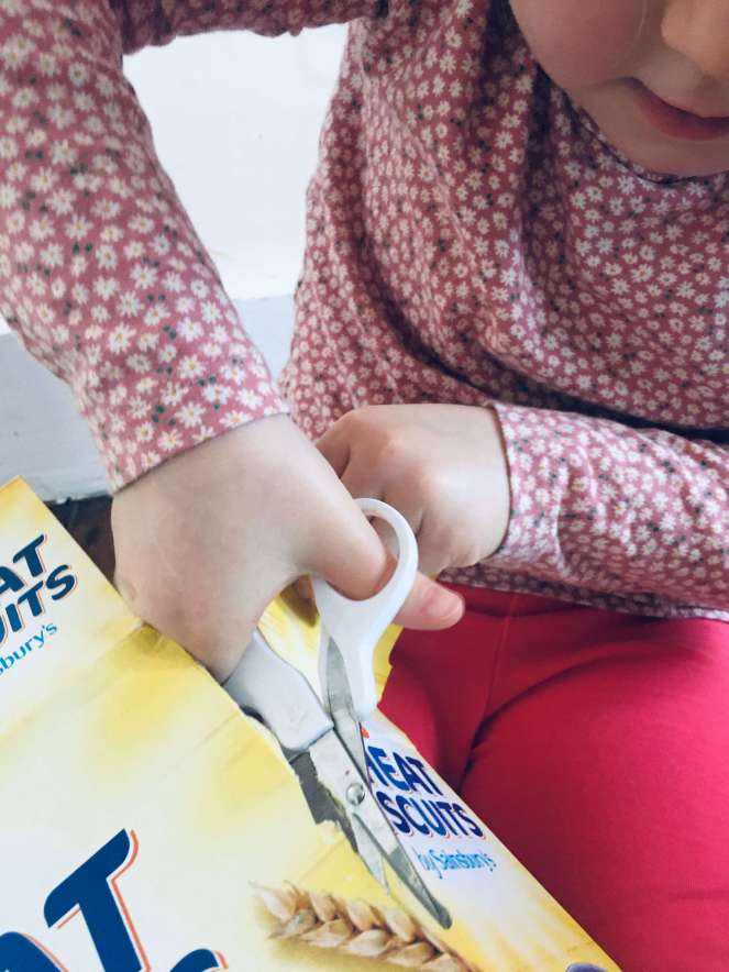 A girl uses a pair of scissors to cut up a cereal packet