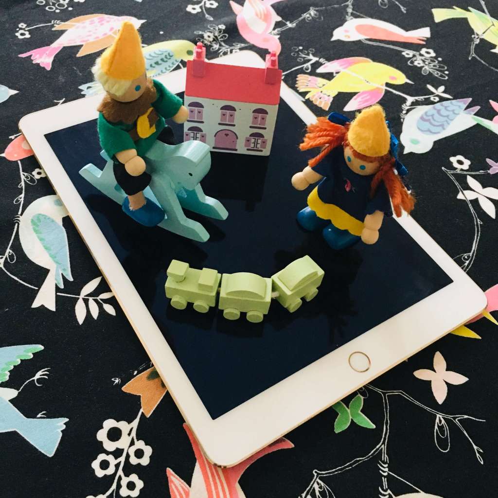 Screen time meets imaginative play - two colourful doll's house wooden dolls are shown playing atop an iPad tablet computer.