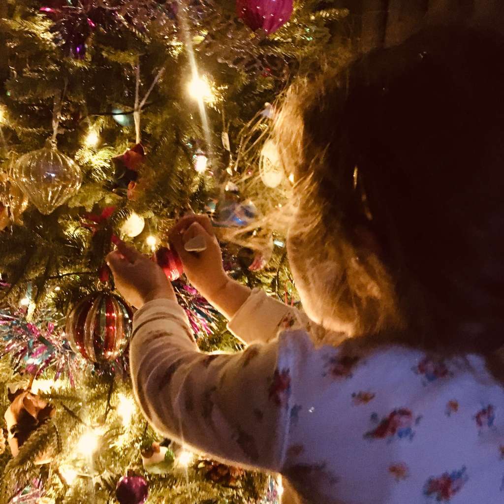 A girl places a Christmas decoration on an illuminated Christmas tree