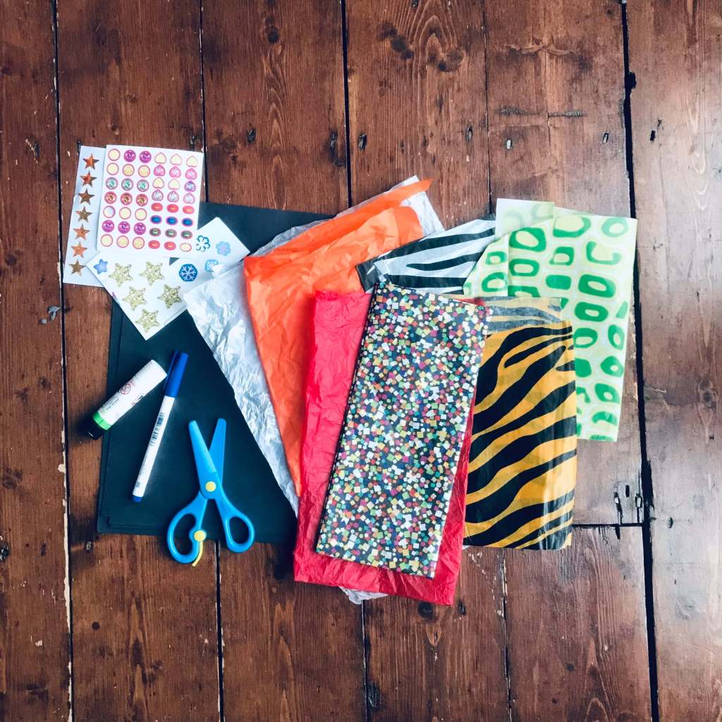 The tools required for a craft activity: black sugar paper, mulitcoloured, tissue paper, scissors, pen, glue and stickers