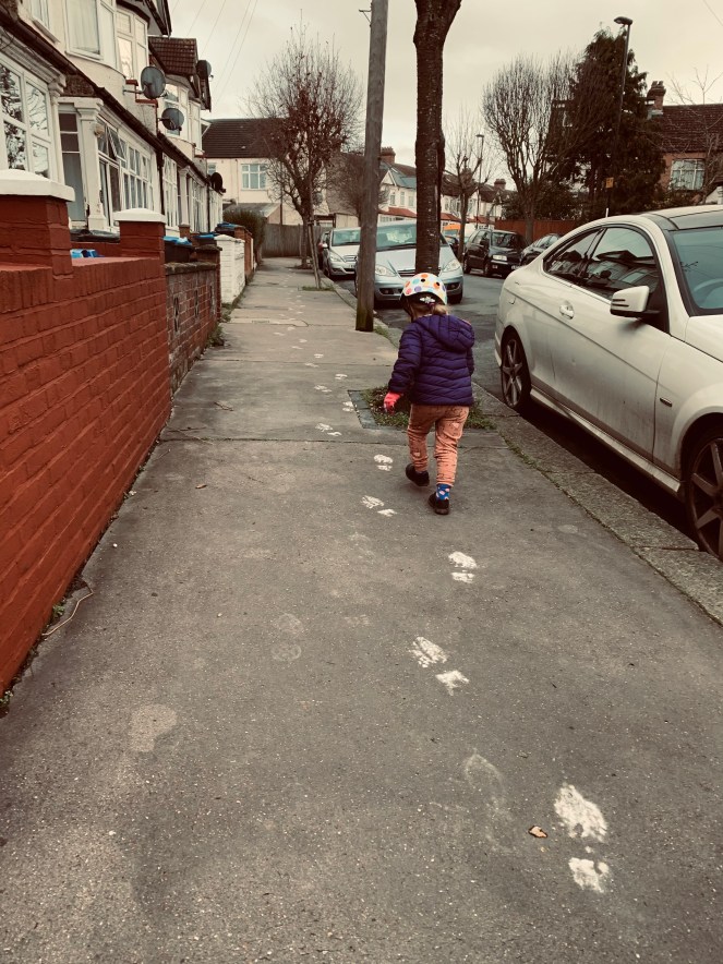 A girl follows a trail of white footprints up a residential street

