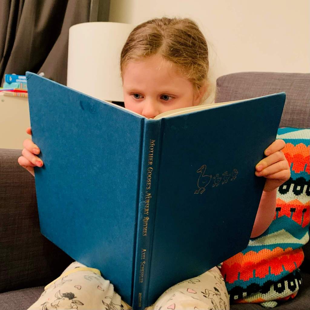 A preschooler sits and reads a book of Nursery Rhymes on her own