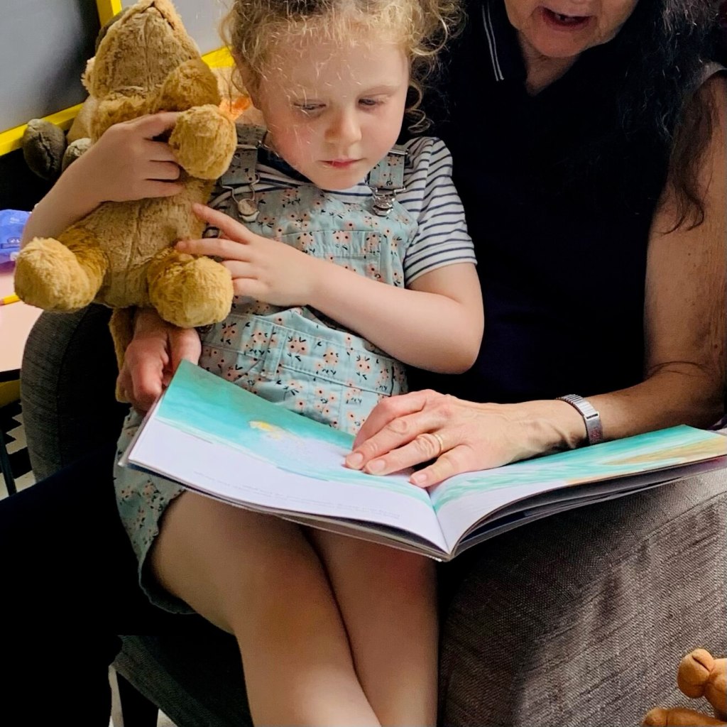 A young child sits on her grandmother's knee to share a picture book together