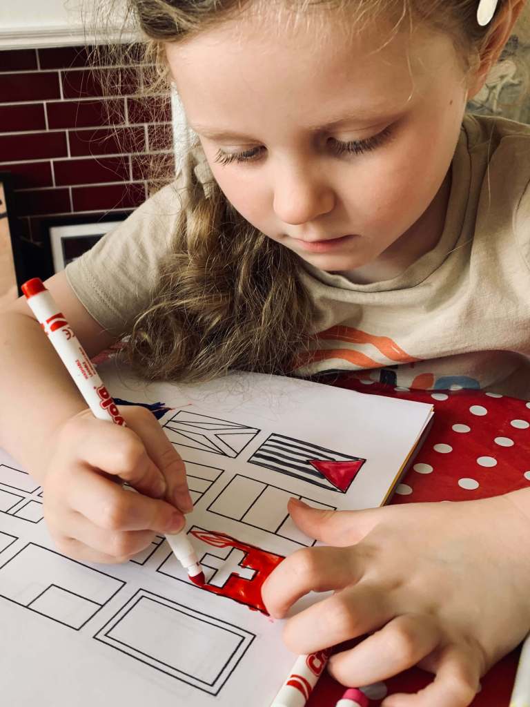 A preschool child uses a felt pen to colour in the national flags on a printable sheet of flags