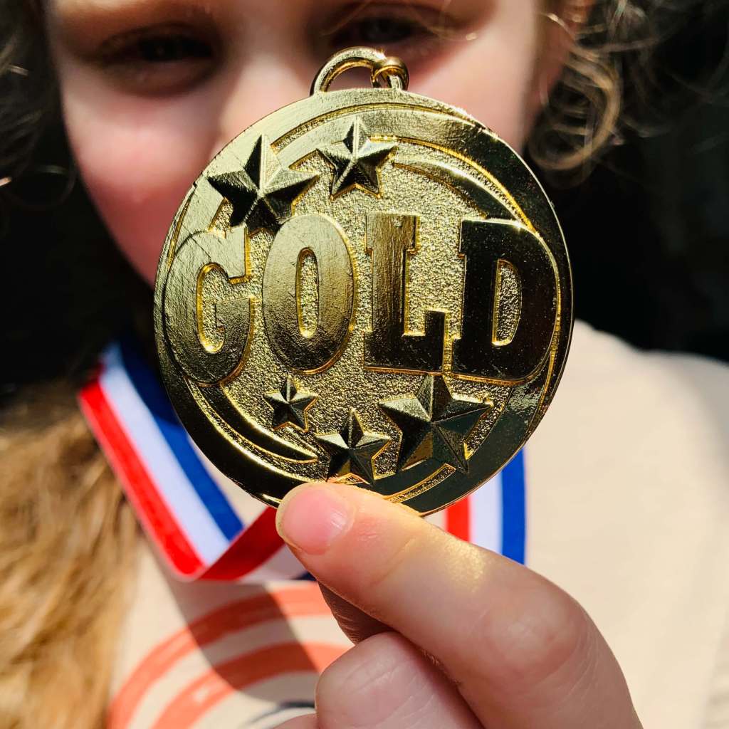 A preschool child holds up a pretend gold medal from her school sports day