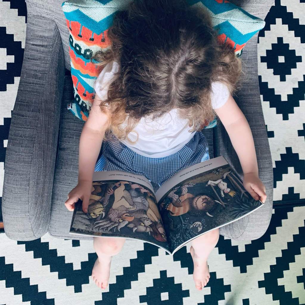 A young child reads a copy of Maurice Sendak's Where the Wild Things Are