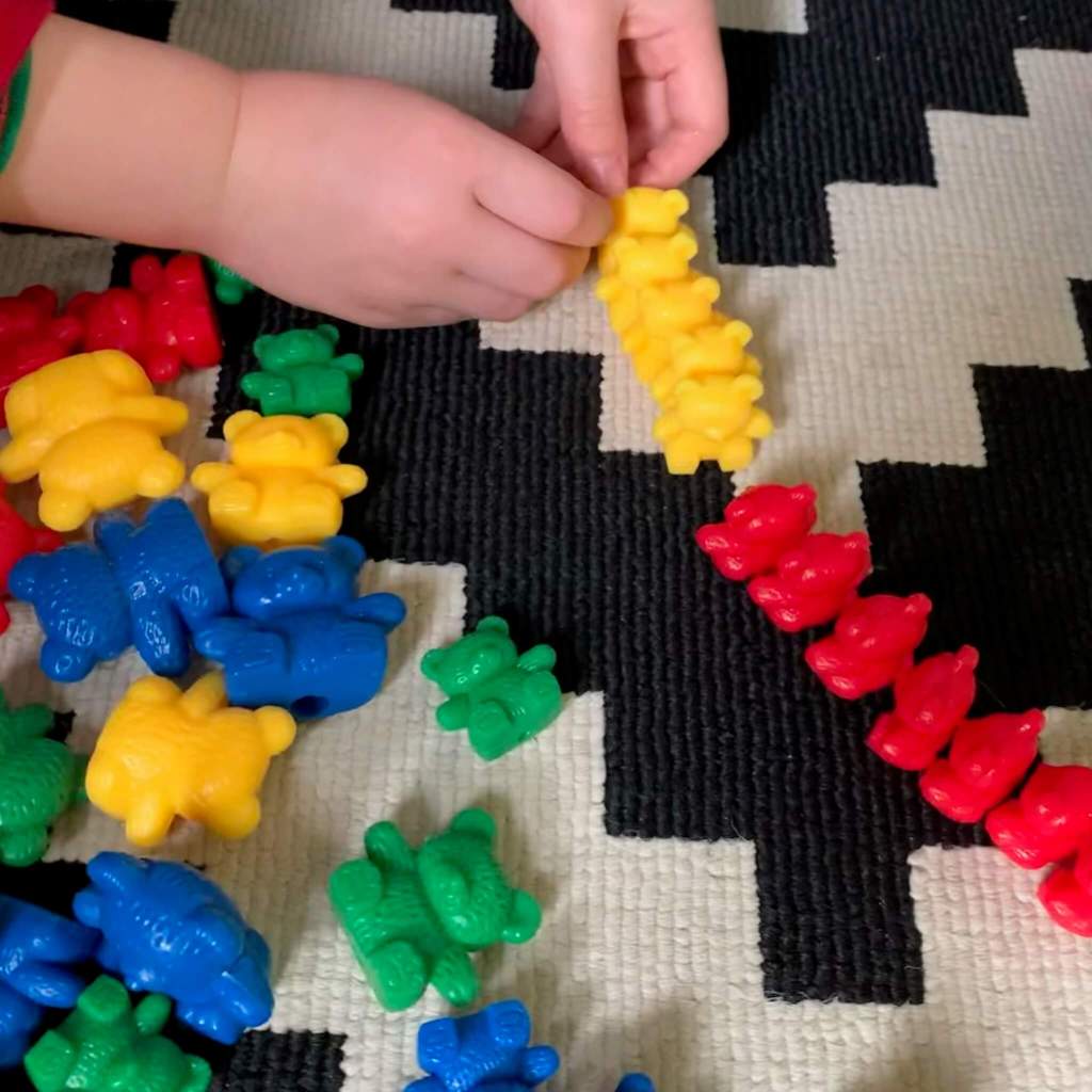 A child plays with a line of compare bears, sorting them into yellow and red groups