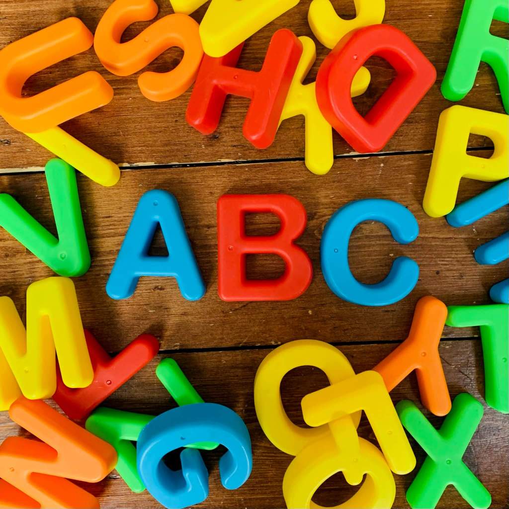 A pile of colourful uppercase plastic letters arranged on the floor, with the first three letters of the Latin alphabet ABC in the centre