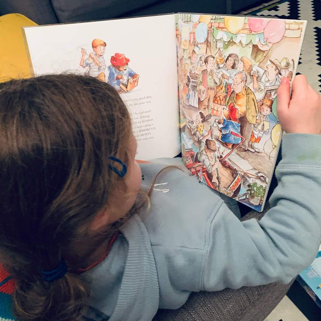 A child reads a copy if Paddington at the Carnival, by Michael Bond with illustrations by R.W. Alley