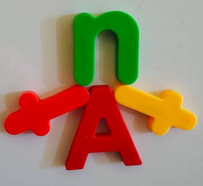 Four magnetic letters arranged to create the vague outline of a person with a capital A for torso and legs, lower case n for a head and two lower case letter t for arms