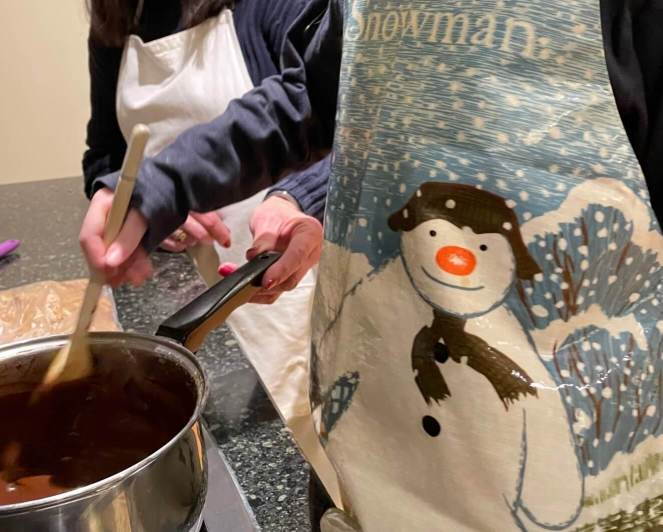 A five year old stirs a pot of melted chocolate while following a Rocky Road recipe, to illustrate an article about getting kids cooking