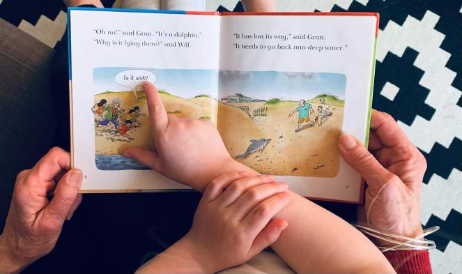 A child points to speech bubble / voice balloon while reading Dolphin Rescue (from the Biff, Chip & Kipper series), with her grandmother