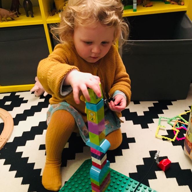 A child builds up a totem-pole-like tower of Duplo blocks