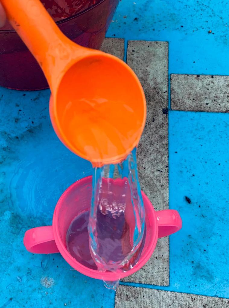 A picture of a young child undergoing a STEM activity, involving transferring water from a large bowl into a smaller cup using a variety of tools: spoons, scoops, a pipette, a funnel and a jug.
