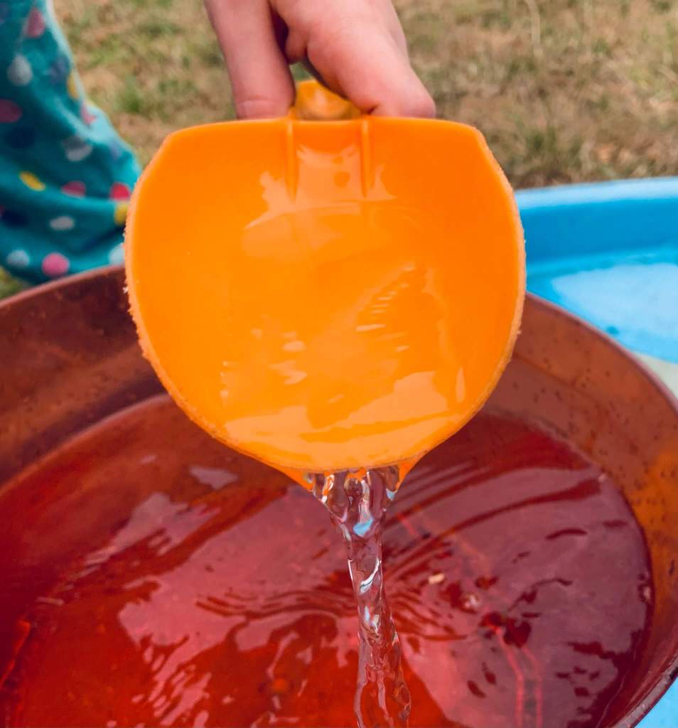 A picture of a young child undergoing a STEM activity, involving transferring water from a large bowl into a smaller cup using a variety of tools: spoons, scoops, a pipette, a funnel and a jug.
