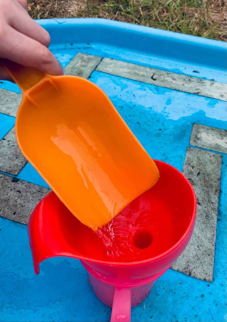 A picture of a young child undergoing a STEM activity, involving transferring water from a large bowl into a smaller cup using a variety of tools: spoons, scoops, a pipette, a funnel and a jug.