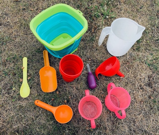 A picture of the tools needed for a STEM activity, involving transferring water from a large bowl into a smaller cup using a variety of tools: spoons, scoops, a pipette, a funnel and a jug.