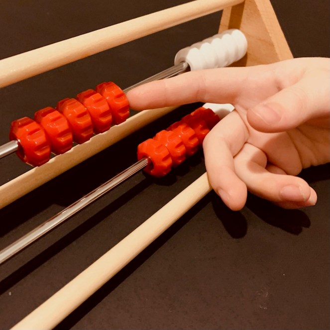 A child slides some beads along the top row of a Dutch counting frame called a rekenrek