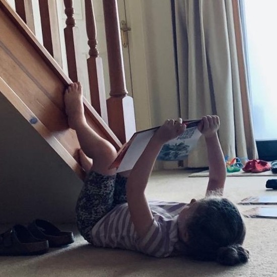 A young child lies on her back, reading a library book held open above her head