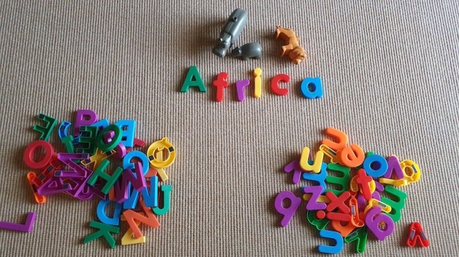 Two piles of lowercase and uppercase magnetic letters on a rug. Above them, the word Africa spelled in sentence case in magnetic letters, alongside several African Duplo animals: a lion and two hippos