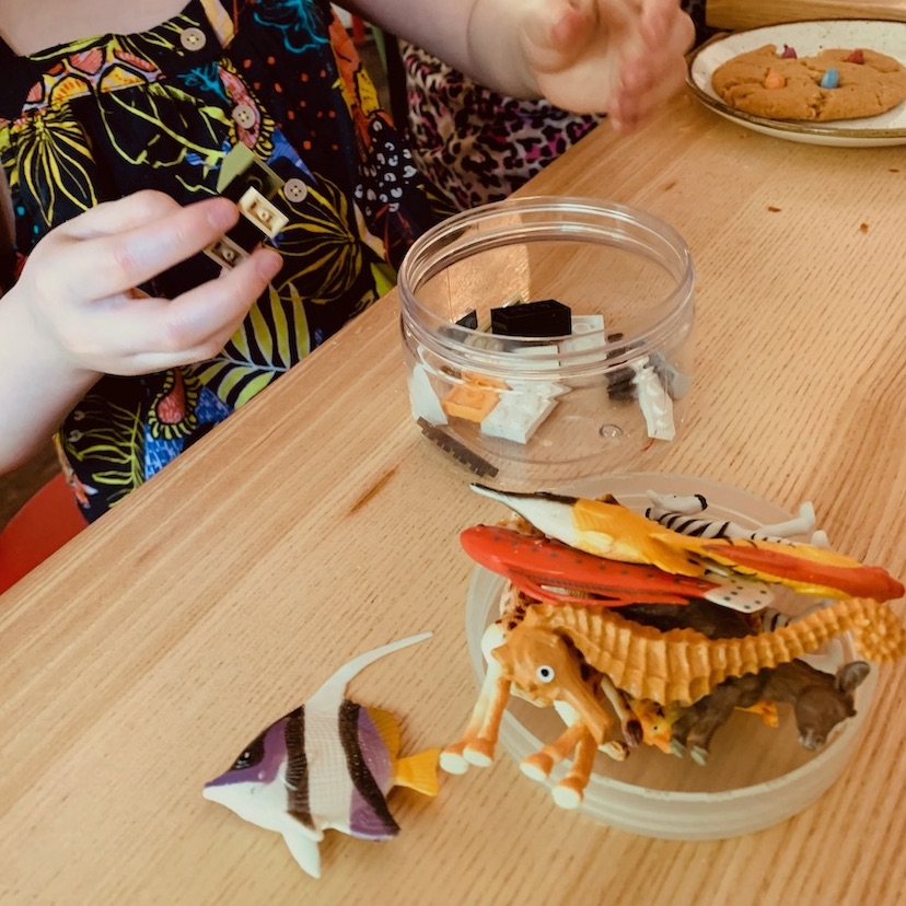 A child handles toys from a collection of miscellaneous toys and Lego spilling from a small plastic pot