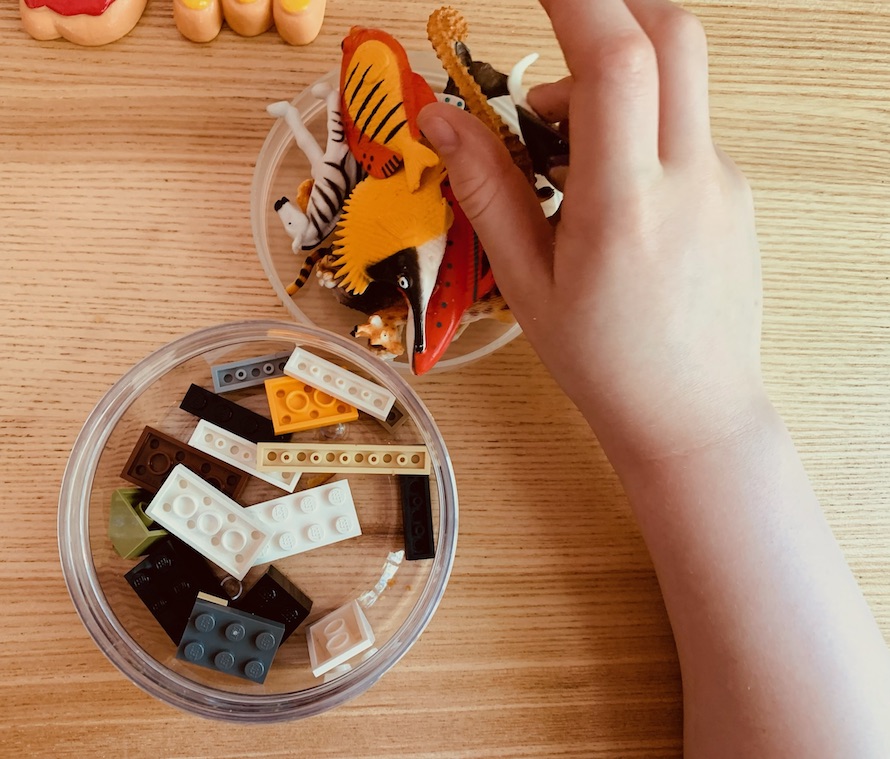 A collection of miscellaneous toys and lego in a small plastic pot and its lid