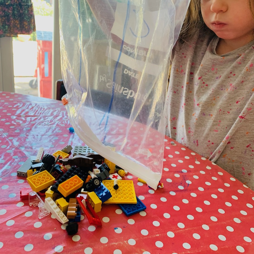 A child finishes emptying a transparent bag of Lego bricks with a number written on the side to recreate the kind of sealed bag that comes in a brand new Lego construction set